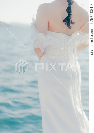 Portrait of a woman in a wedding dress standing in the backlight at the beach Portrait of a woman in a wedding dress standing in the backlight at the beach 126258819