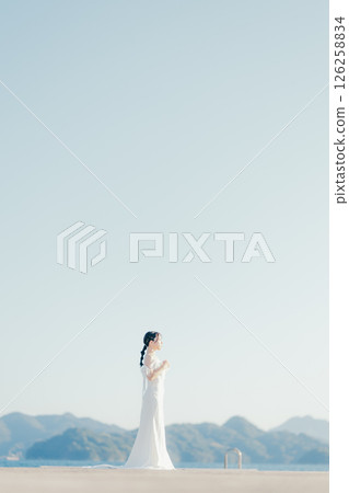 Portrait of a woman in a wedding dress standing in the backlight at the beach Portrait of a woman in a wedding dress standing in the backlight at the beach 126258834