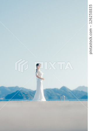 Portrait of a woman in a wedding dress standing in the backlight at the beach 126258835
