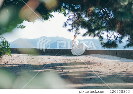 一位身穿婚紗的女子坐在陽光下，背景是一座山 126258863