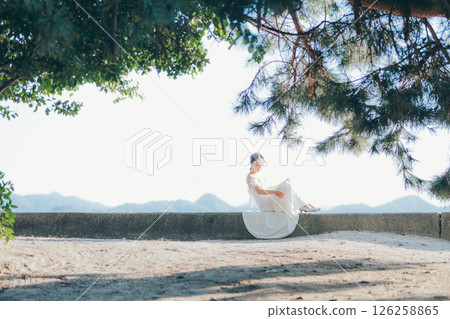 A woman in a wedding dress sitting in the sunlight with a mountain in the background A woman in a wedding dress sitting in the sunlight with a mountain in the background 126258865