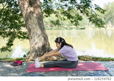 Wellness and Self-Care. A woman doing yoga stretches outdoors by a serene lake. Wellness and Self-Care. A woman doing yoga stretches outdoors by a serene lake. 126259762