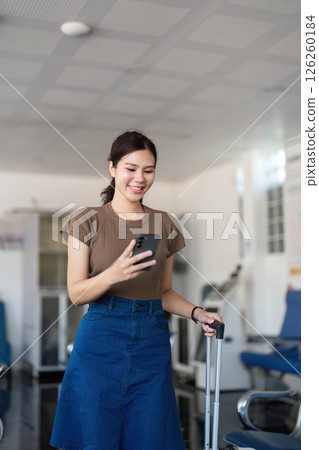 Travel woman looking at phone with suitcase while walking in airport Travel woman looking at phone with suitcase while walking in airport 126260184
