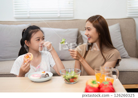 Wellness and healthy eating: Mother playfully feeding daughter a salad Wellness and healthy eating: Mother playfully feeding daughter a salad 126260325