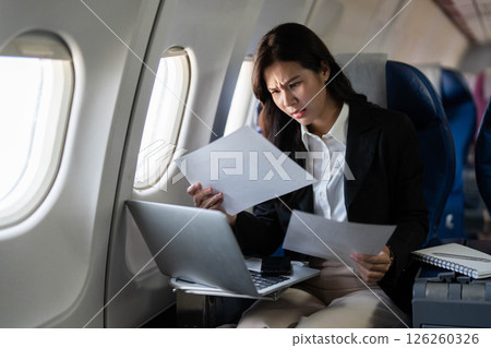 Business travel: Concerned professional woman evaluating documents on airplane Business travel: Concerned professional woman evaluating documents on airplane 126260326