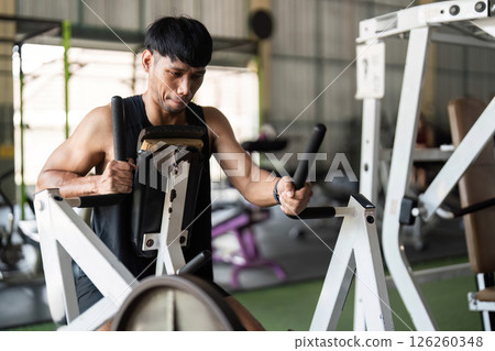 Fitness Commitment. Young man performing strength training on gym equipment for muscle enhancement. 126260348