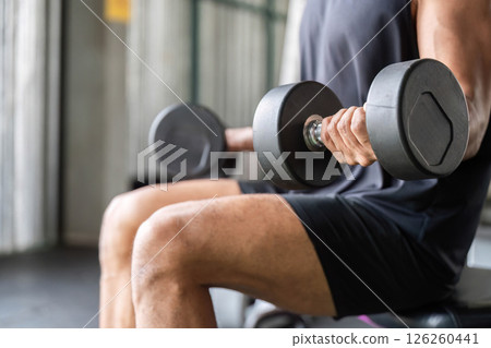 Focused Fitness Routine: Man Lifting Dumbbells while Seated. 126260441