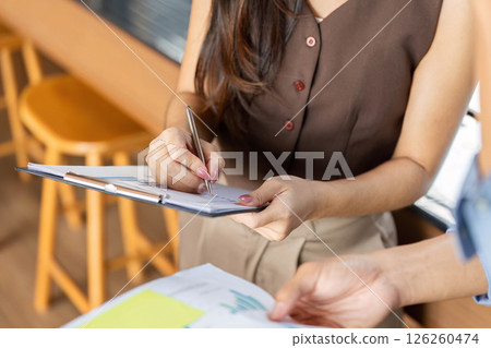 Business Documentation and Note-taking. Professional woman signing documents in a modern office. Business Documentation and Note-taking. Professional woman signing documents in a modern office. 126260474