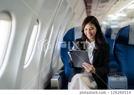 Business travel with young woman smiling while using tablet on airplane Business travel with young woman smiling while using tablet on airplane 126260514