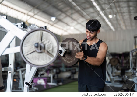 Fitness Focus. Young man engaging in weightlifting for strength enhancement in gym. Fitness Focus. Young man engaging in weightlifting for strength enhancement in gym. 126260517