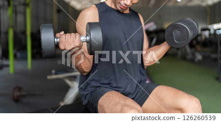 Fitness Focus. Young man lifting dumbbells for strength training in gym. 126260539