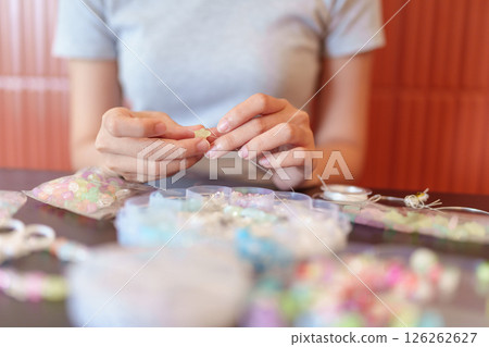 Young woman creating handmade beaded jewelry as a relaxing DIY craft activity at cozy home table 126262627