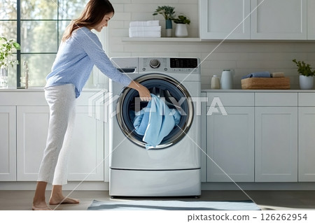 Housewife loading clothes into washing machine in laundry room Housewife loading clothes into washing machine in laundry room 126262954