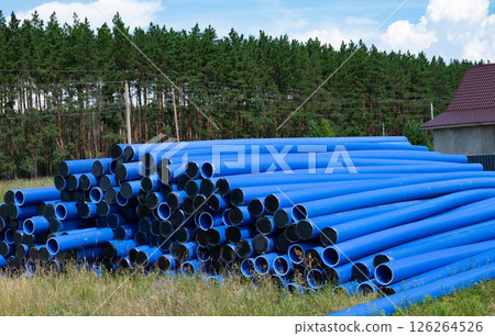 Stacked blue pipes resting in a field near a forest during daylight Stacked blue pipes resting in a field near a forest during daylight 126264526