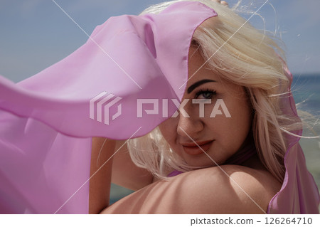 Blonde woman beach: Woman poses at beach, covers her face with pink fabric, sunny day. 126264710