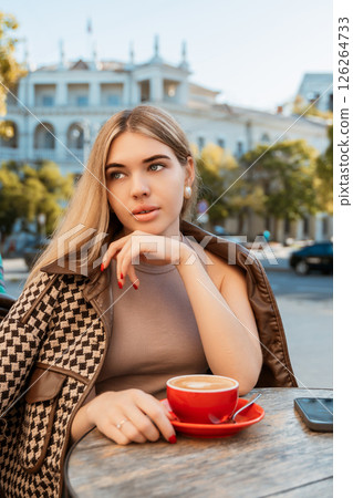 Woman Coffee Cafe - A young woman sits at a table outside a cafe, enjoying a cup of coffee. 126264733