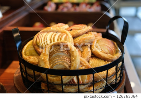 Crispy apple strudels, pastries, with a sugar-coated surface arranged in a woven basket lined with white paper, accompanied by a cup of warm tea and a lit candle. 126265364