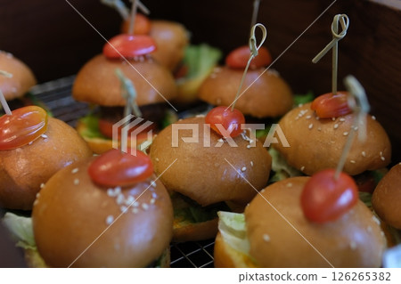 mini burgers set with sesame seed buns, lettuce, and cooked patties stacked on a serving tray. mini burgers set with sesame seed buns, lettuce, and cooked patties stacked on a serving tray. 126265382