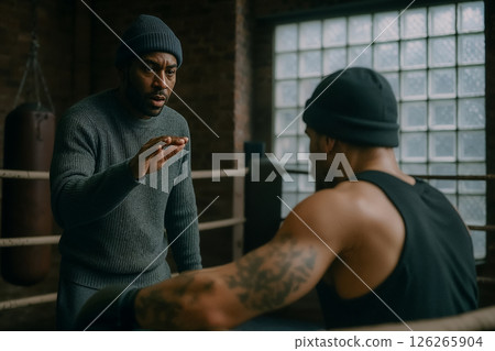 Instructions in boxing gym, experienced trainer instructs athlete developing sparring strategy, background of gym in retro style, gestures of trainer explain training strategy, moment of mentoring Instructions in boxing gym, experienced trainer instructs athlete developing sparring strategy, background of gym in retro style, gestures of trainer explain training strategy, moment of mentoring 126265904