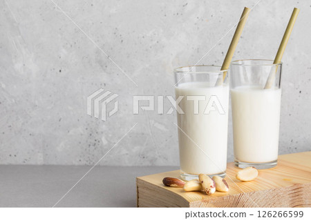 Brazil nut milk in two glasses with bamboo straws on wooden surface against textured background 126266599