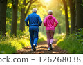 Gray-haired grandparents in pink and blue tracksuit jogging in the park, in the background in blurred green trees 126268038