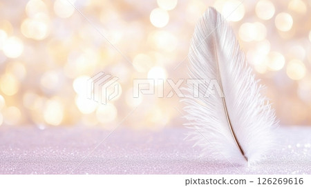 White feather standing on glittering surface with golden bokeh background gently swaying in the breeze, symbolizing lightness, peace and angelic presence 126269616