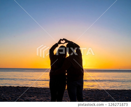 A silhouette of love on the beach at dusk: The sun setting on the horizon and the trail of a heart - The eternal vows of two people 126271873