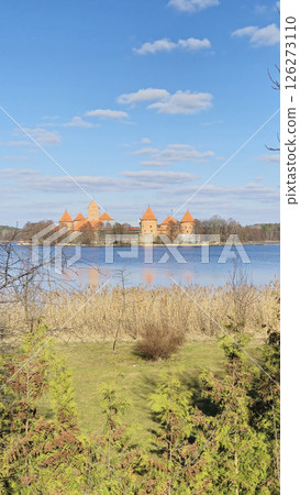 Trakai Lithuania - 03.28.2025 Trakai Island Castle with orange towers reflected in the still lake, surrounded by reeds and spring greenery under a bright blue sky Trakai Lithuania - 03.28.2025 Trakai Island Castle with orange towers reflected in the still lake, surrounded by reeds and spring greenery under a bright blue sky 126273110