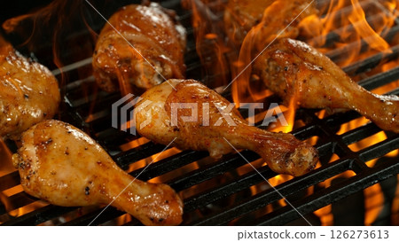 Close-up of Delicious Chicken Legs on a Grill with Roaring Flames 126273613
