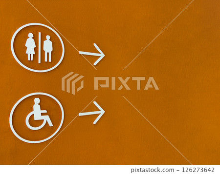 Modern restroom direction sign with male, female and wheelchair symbols on bold orange wall, pointing to the right. Accessible and inclusive design for public facilities navigation 126273642