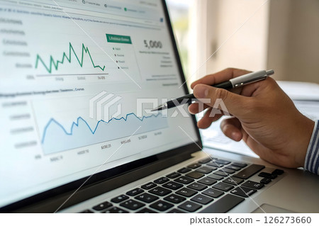 Business professional analyzing financial charts and graphs on laptop screen while holding pen, data analysis and market research, investment strategy and business intelligence 126273660