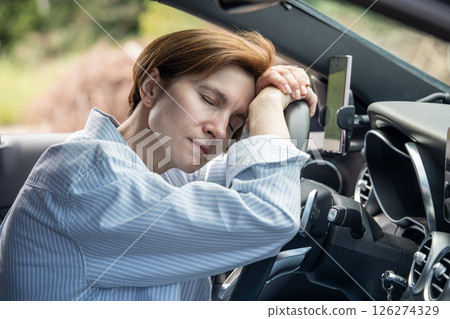 Middle aged tired woman sleeping on steering wheel exhausted from long driving in road trip. Middle aged tired woman sleeping on steering wheel exhausted from long driving in road trip. 126274329
