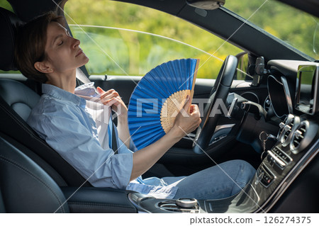 Overheated exhausted middle aged woman driver with hand fan suffering from heat in car. Hot weather  126274375