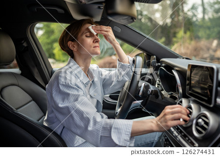 Woman drives car with broken air conditioner in hot weather wipes sweat on face. Woman drives car with broken air conditioner in hot weather wipes sweat on face. 126274431