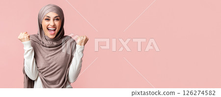 Joy Of Victory. Happy Muslim Woman in Hijab Shaking Fists Celebrating Success Over Pink Studio Background, Empty Space 126274582