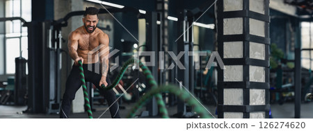 Crossfit training. Naked muscular man exercising with battle ropes at gym, free space, panorama Crossfit training. Naked muscular man exercising with battle ropes at gym, free space, panorama 126274620