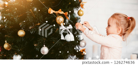 Mother's helper. Little baby girl decorating Christmas tree at home, side view 126274636