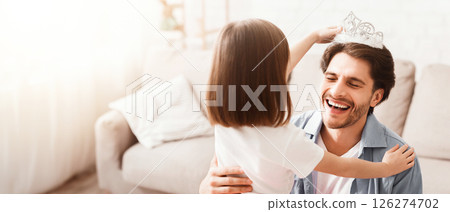 Little girl putting crown on her laughing dad head, having fun together at home, close up Little girl putting crown on her laughing dad head, having fun together at home, close up 126274702