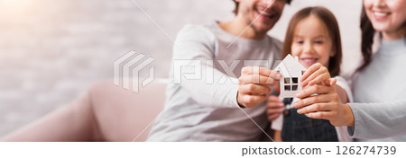 Family Housing And Adoption Concept. Cutout Paper House In Hands Of Happy Family Of Three With Little Daughter, Selective Focus Family Housing And Adoption Concept. Cutout Paper House In Hands Of Happy Family Of Three With Little Daughter, Selective Focus 126274739