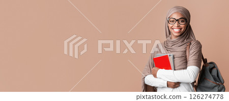 Education Concept. Portrait Of Smiling Black Muslim Girl In Hijab With Backpack And Notepads Posing Over Yellow Background With Empty Space Education Concept. Portrait Of Smiling Black Muslim Girl In Hijab With Backpack And Notepads Posing Over Yellow Background With Empty Space 126274778
