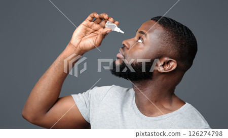 Black guy applying ophthalmology eyedropper. Glaucoma eye prevention, human vision serum wash Black guy applying ophthalmology eyedropper. Glaucoma eye prevention, human vision serum wash 126274798
