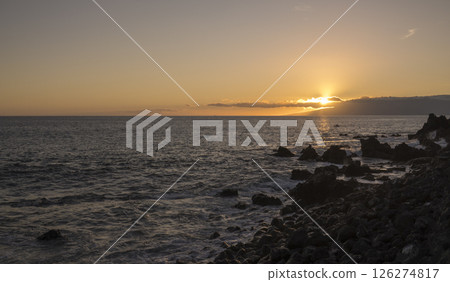 Orange sunset at sea shore promenade in Playa de San Juan, Tenerife, Spain in the south of Tenerife with ocean waves crushing black lava rocks 126274817