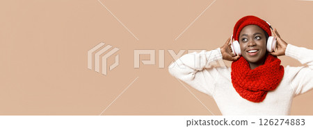 Playful young african woman in wireless headphones listening to music and dancing, beige background 126274883