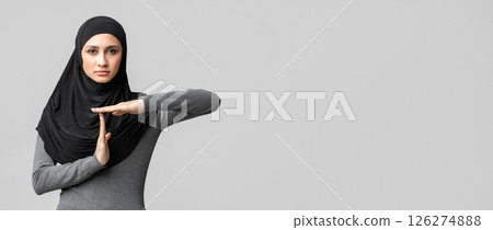 Serious muslim woman in hijab showing time out gesture, demonstrating time break sign over gray background and looking at camera, free space 126274888