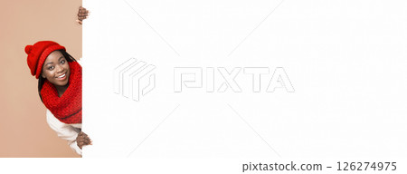 Empty Space For Advertising. Black cheerful woman in red knitted set staying next to empty beige board, beige background 126274975
