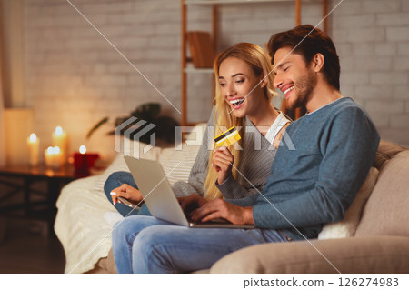 Online Banking. Happy Spouses Using Laptop And Credit Card Doing Internet Shopping Sitting On Sofa At Home. Selective Focus 126274983