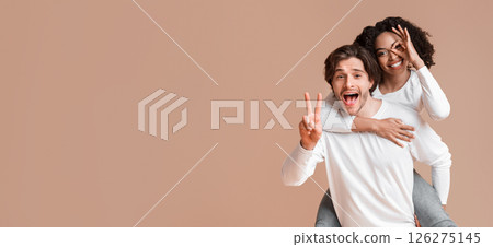 Interracial couple fooling together and showing funny gestures. Cheerful guy piggybacking his afro girlfriend, having fun over yellow background Interracial couple fooling together and showing funny gestures. Cheerful guy piggybacking his afro girlfriend, having fun over yellow background 126275145