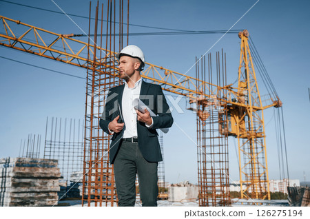 In hard hat, holding plan in hands. Businessman in formal clothes is on the construction site at daytime 126275194