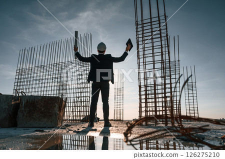 With hands up. Standing at evening time. Businessman in formal clothes is on the construction site With hands up. Standing at evening time. Businessman in formal clothes is on the construction site 126275210