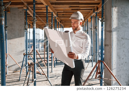 In shirt and black pants. Reading the plan. Man is working on the construction site at daytime 126275234